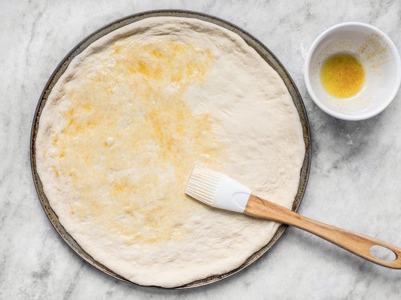 Brush Garlic Oil onto stretched pizza dough