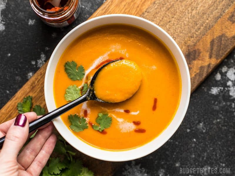 Overhead view of a bowl of Thai Coconut Curry Carrot Soup with a hand lifting a spoonful