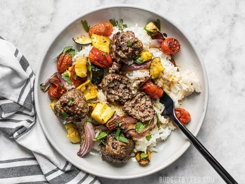 Beef Kofta Meatballs with Roasted Vegetables on a stoneware plate with a black fork and striped napkin