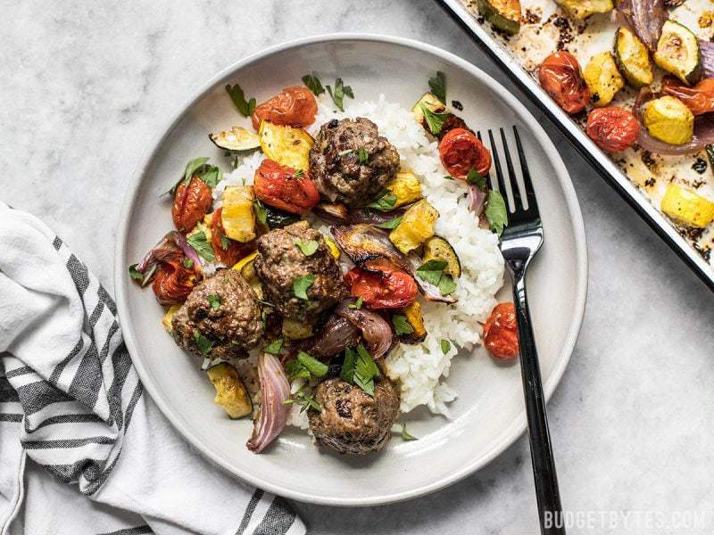 Beef Kofta Meatballs with Roasted Vegetables are the perfect well-rounded easy dinner or meal prep to keep you fed and happy throughout the week. BudgetBytes.com Beef Kofta Meatballs with Roasted Vegetables on a plate next to the roasting sheet pan