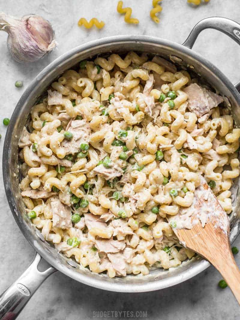 A large skillet full of Creamy Tuna Pasta with Peas and Parmesan with a wooden spatula