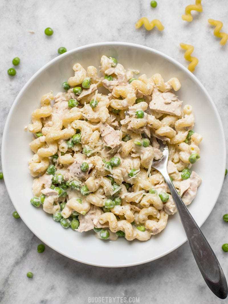 A white bowl of Creamy Tuna Pasta with Peas and Parmesan with a fork