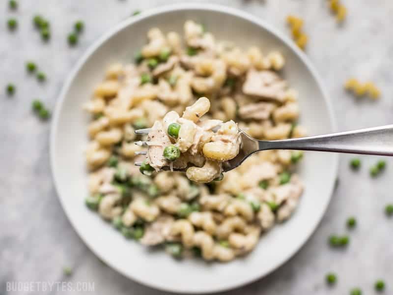 Close up view of a forkful of Creamy Tuna Pasta with Peas and Parmesan with the bowl in the background 