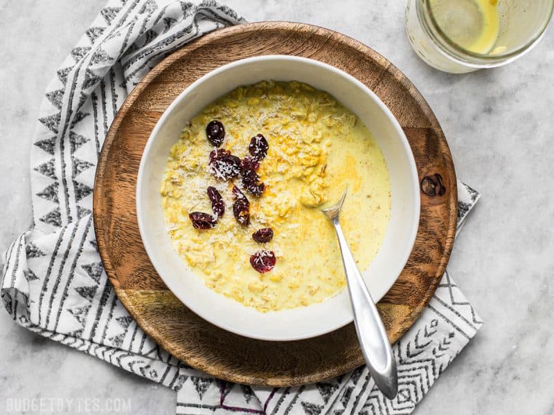 A spoon sitting in a bowl of Golden Milk Overnight Oats with dried cranberries and coconut. 