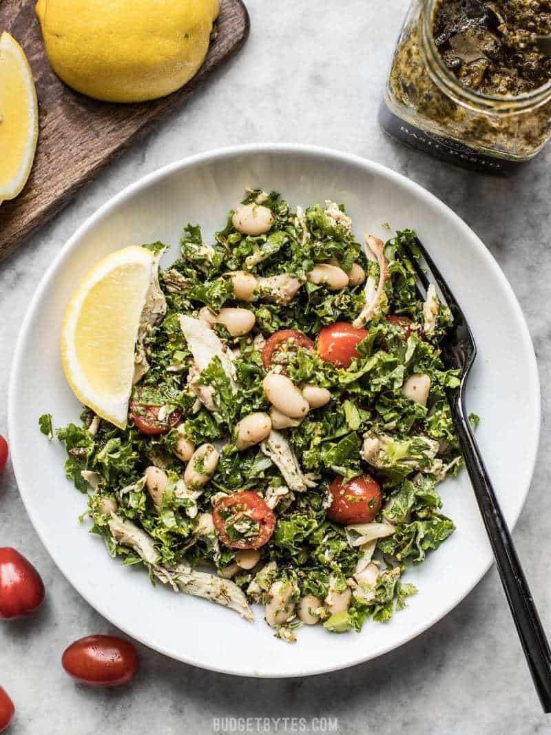 A large bowl of Kale White Bean and Pesto Salad with lemon wedges and a black fork.
