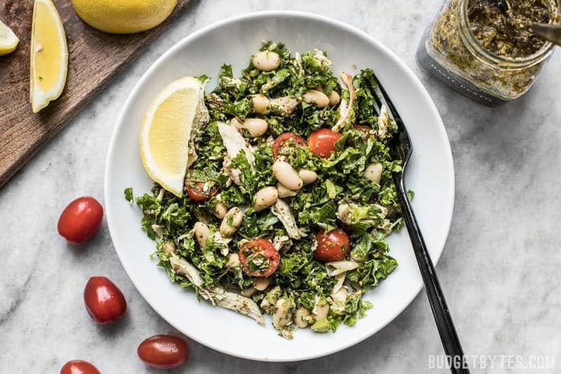 A plate of Kale White Bean and Pesto Salad with lemons on the side and a jar of pesto