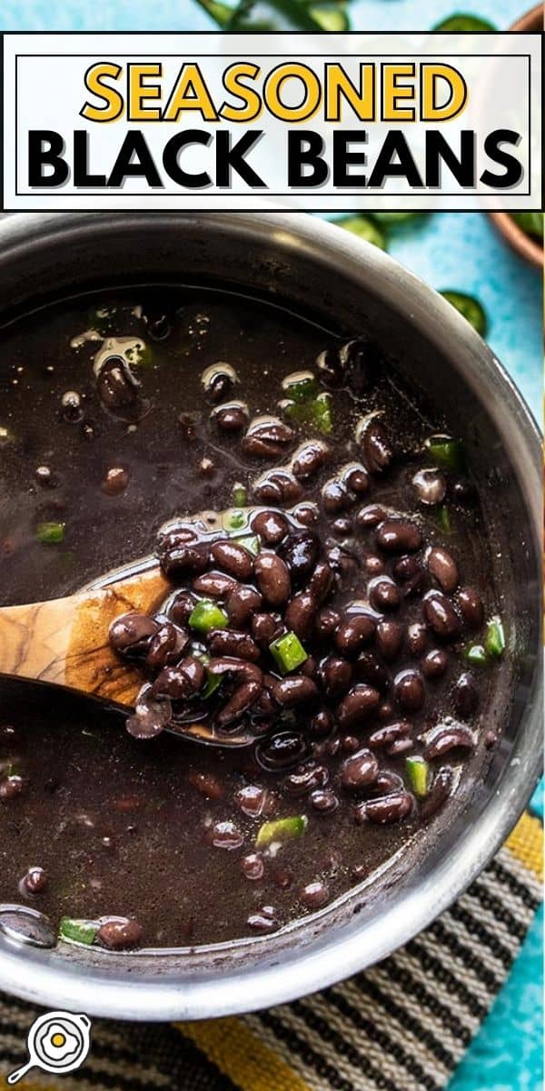 Close up overhead view of black beans in a pot being lifted with a wooden spoon.