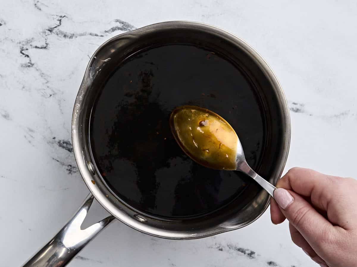Teriyaki sauce cooking in a sauce pan, with a spoon coated in the sauce to check the thickness.