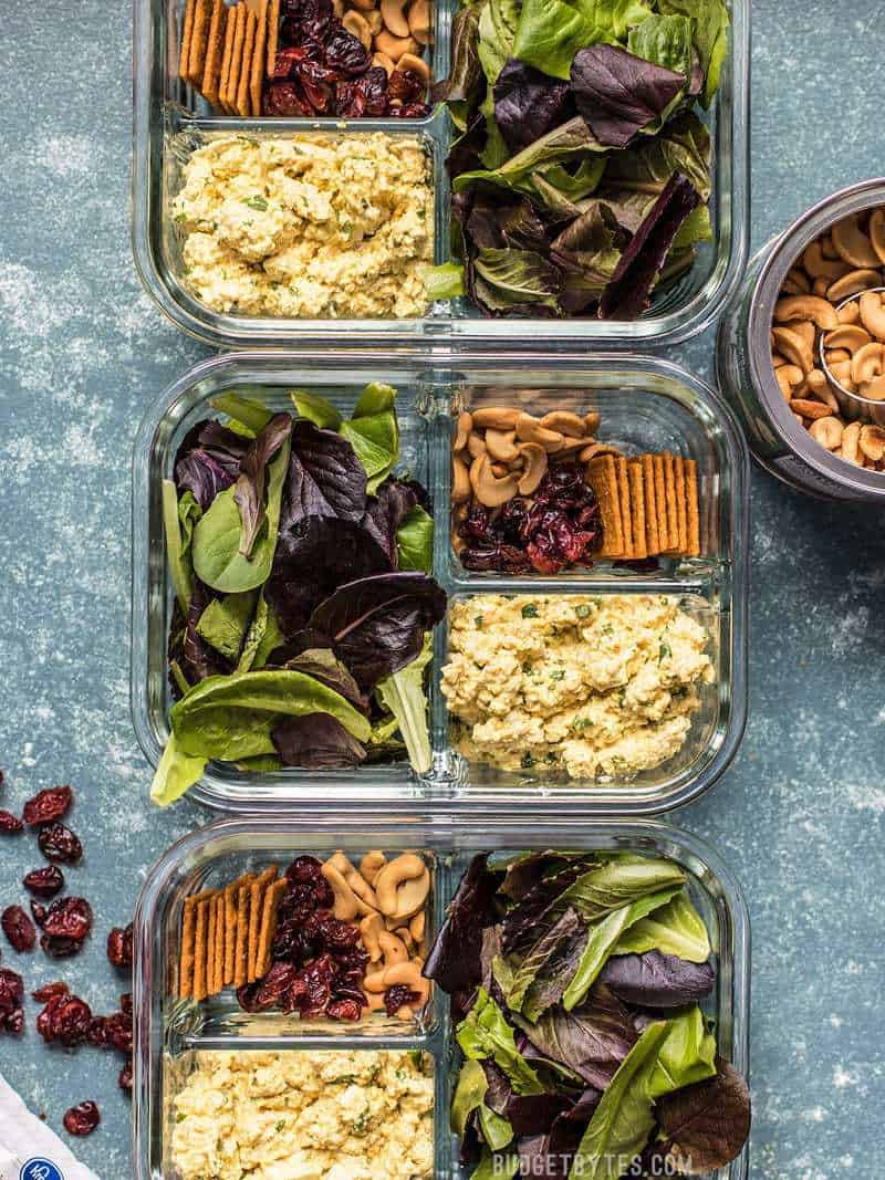 Three Curried Tofu Salad Meal Prep containers with dried cranberries and cashews on the sides