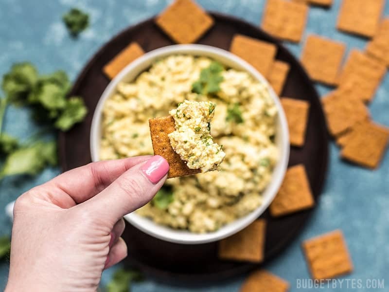 Close up of Curried Tofu Salad on a cracker, being held in a hand.