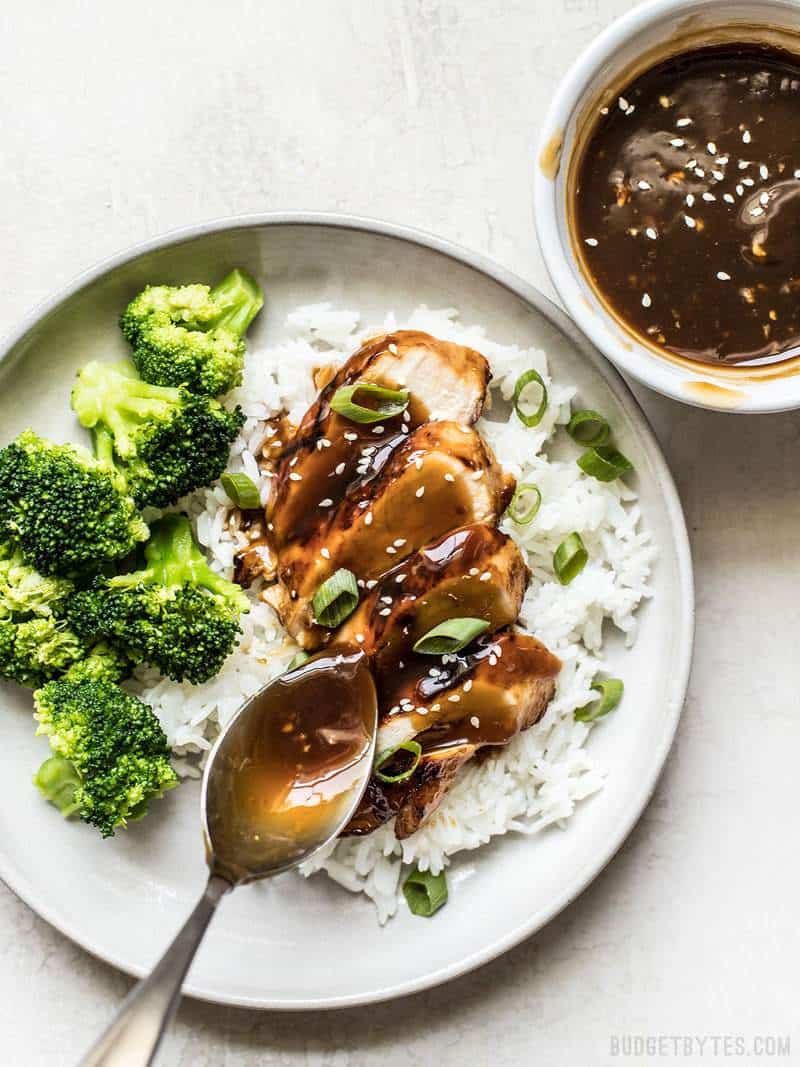 Teriyaki Sauce being spooned over sliced chicken on a plate with rice and broccoli
