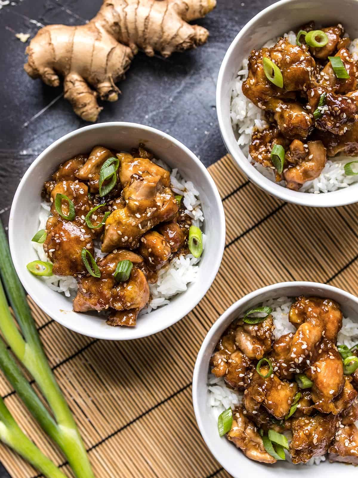 Three bowls of sesame chicken with rice and green onions.