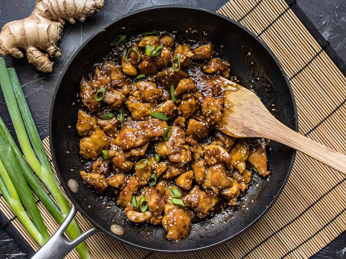Overhead view of a frying pan full of sesame chicken with a wooden spatula.