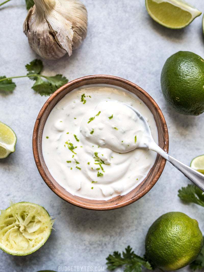 A bowl of Lime Crema surrounded by garlic, limes, and cilantro