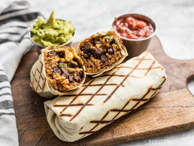 A bean and cheese burrito cut open to show the inside, next to cups of guacamole and salsa. 