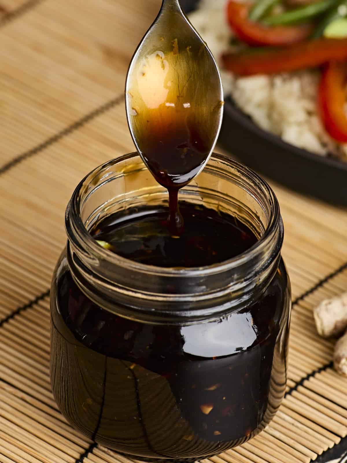 Side view of a glass jar of easy homemade teriyaki sauce, with a spoon dipped in.