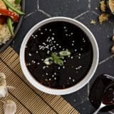 Overhead view of a bowl of homemade teriyaki sauce, topped with sesame seeds and sliced green onion.