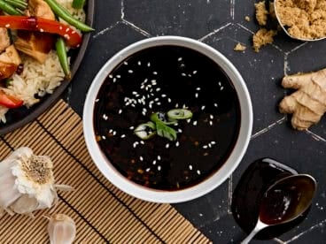 Overhead view of a bowl of homemade teriyaki sauce, topped with sesame seeds and sliced green onion.