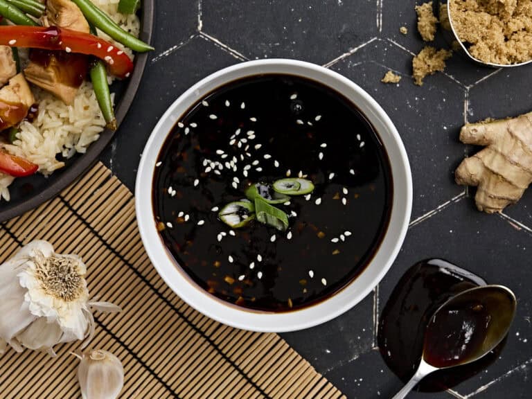 Overhead view of a bowl of homemade teriyaki sauce, topped with sesame seeds and sliced green onion.