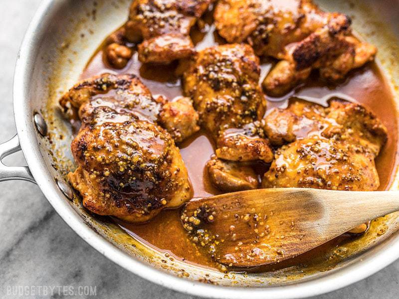 Close up of honey mustard chicken in the skillet with a wooden spoon scooping the pan sauce. 