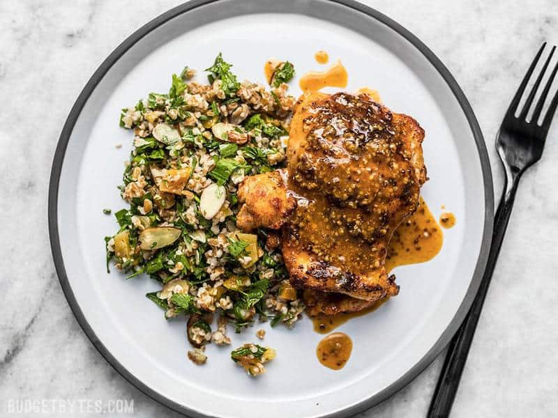 A plate of honey mustard chicken with pan sauce drizzled over top and parsley almond salad on the side. 