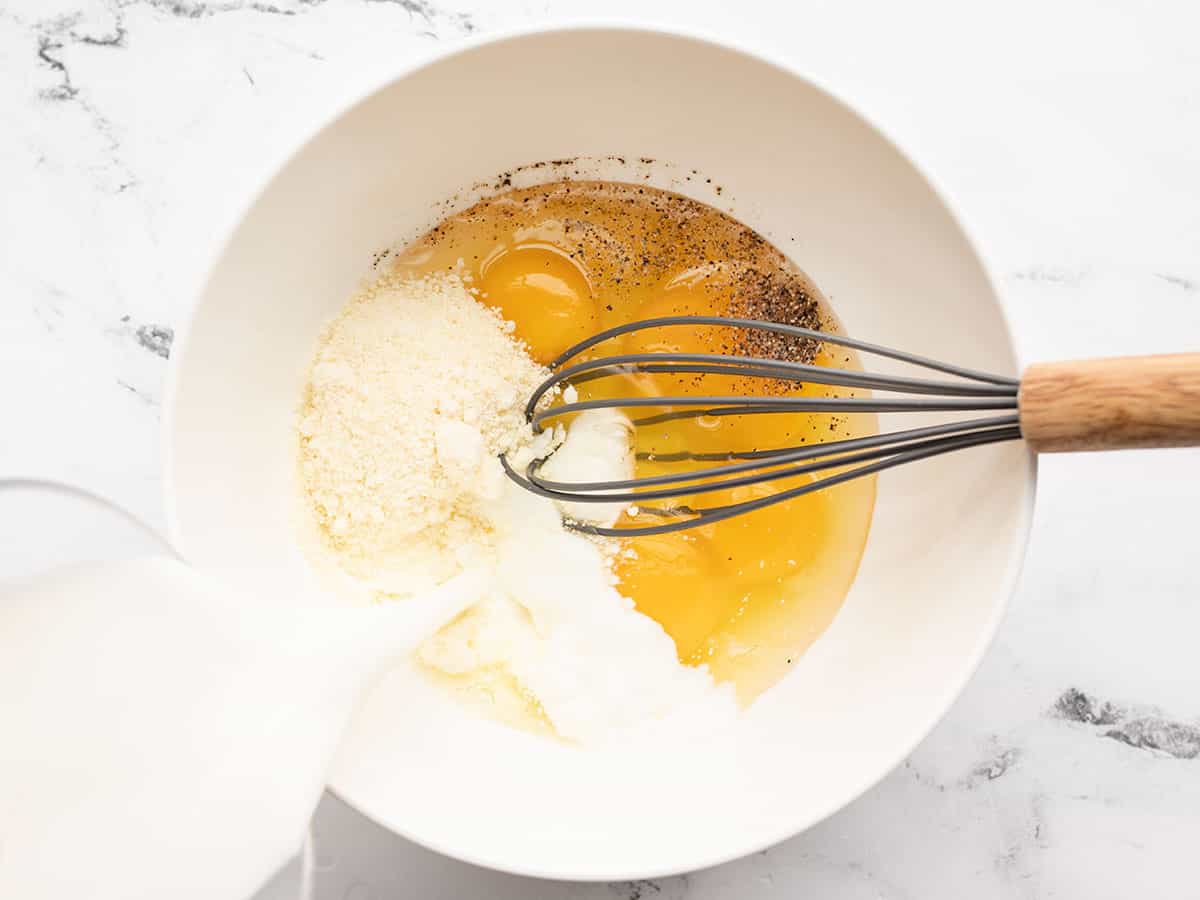 Milk being poured into a bowl with eggs, Parmesan, and pepper