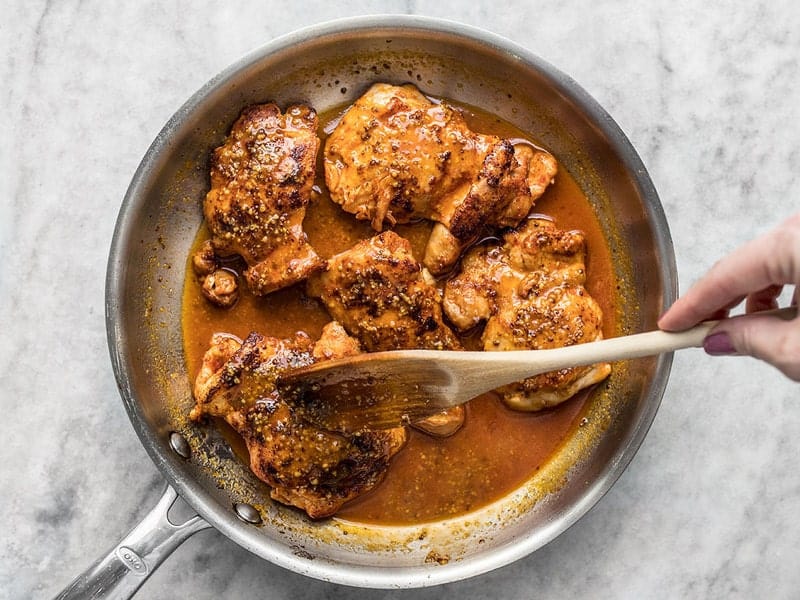 Honey mustard pan sauce being drizzled over chicken thighs in the skillet