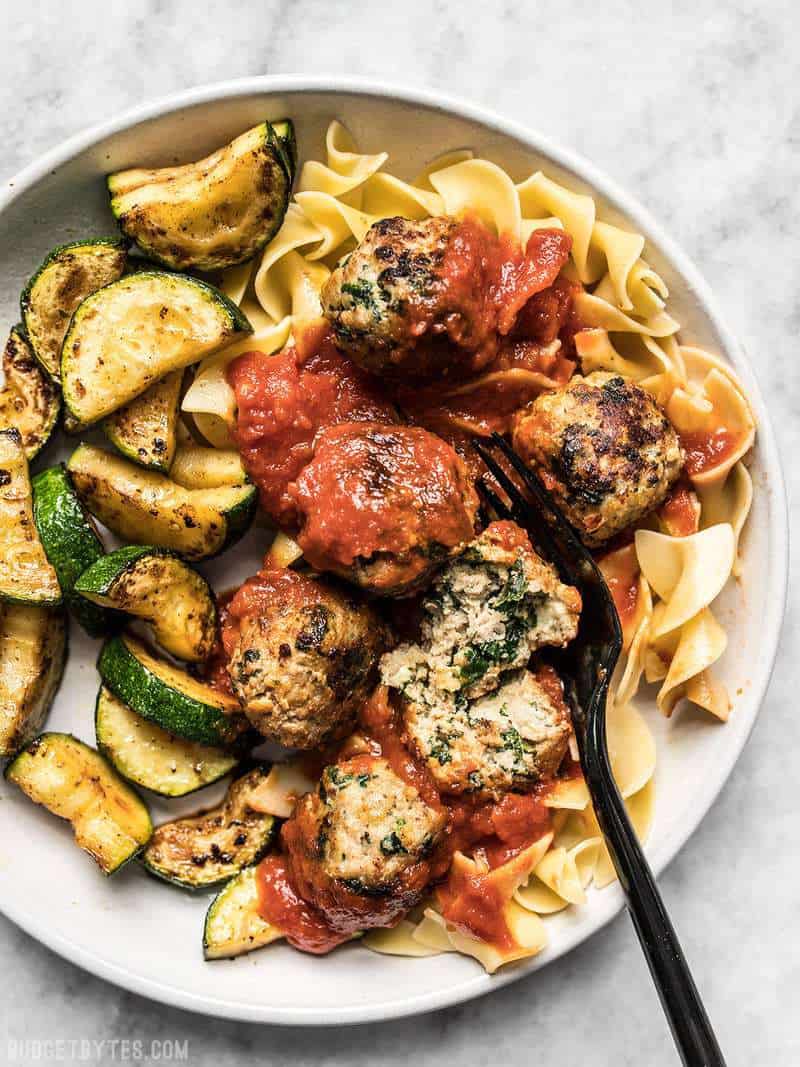 A large plate full of Spinach and Feta Turkey Meatballs with marinara, pasta, and sautéed zucchini. 