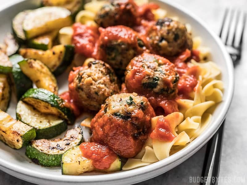 Front view of a plate full of Spinach and Feta Turkey Meatballs with marinara, vegetables, and pasta.