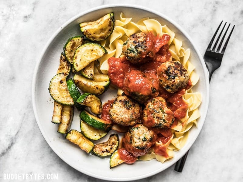 A fixed plate of Spinach and Feta Turkey Meatballs with marinara, vegetables, and pasta