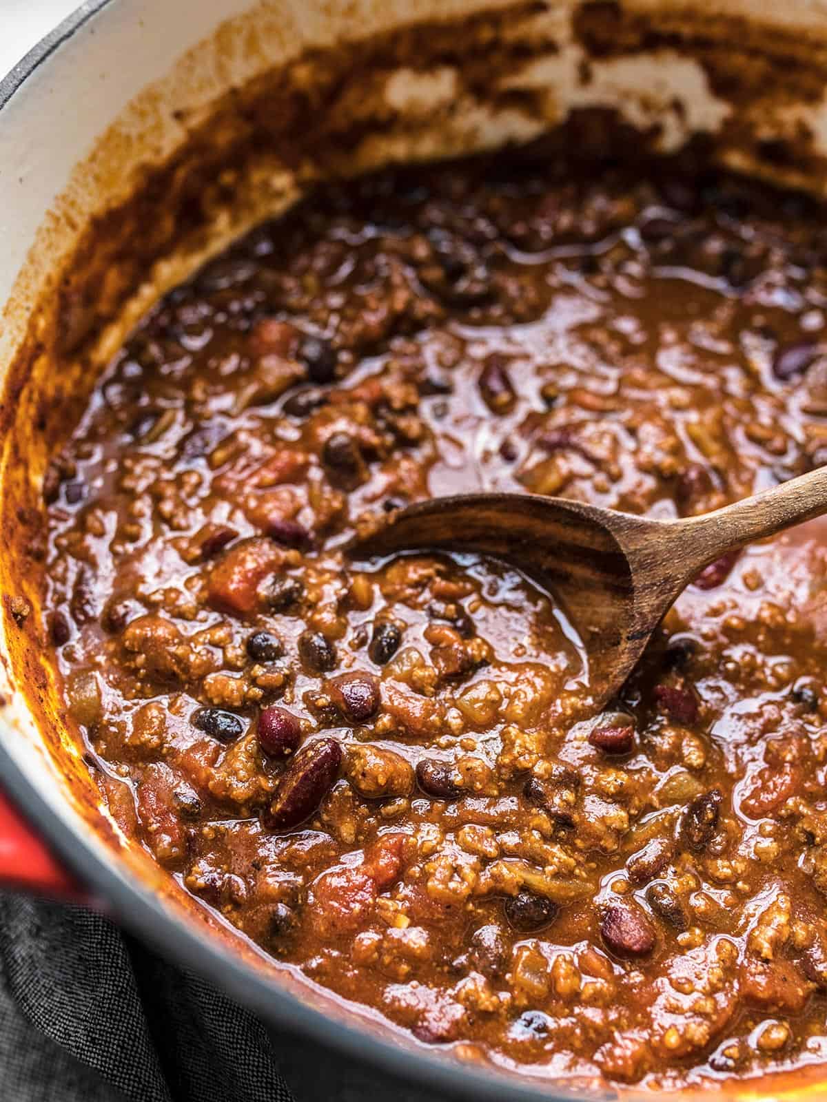 Close up side view of a pot of chili with a wooden spoon.