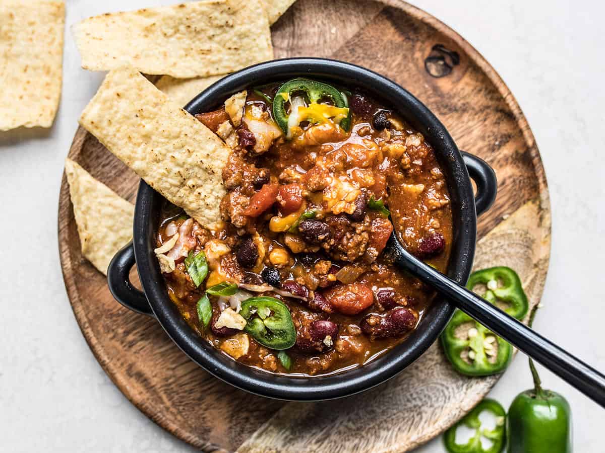 Overhead view of a bowl full of chili with toppings and a spoon in the center.