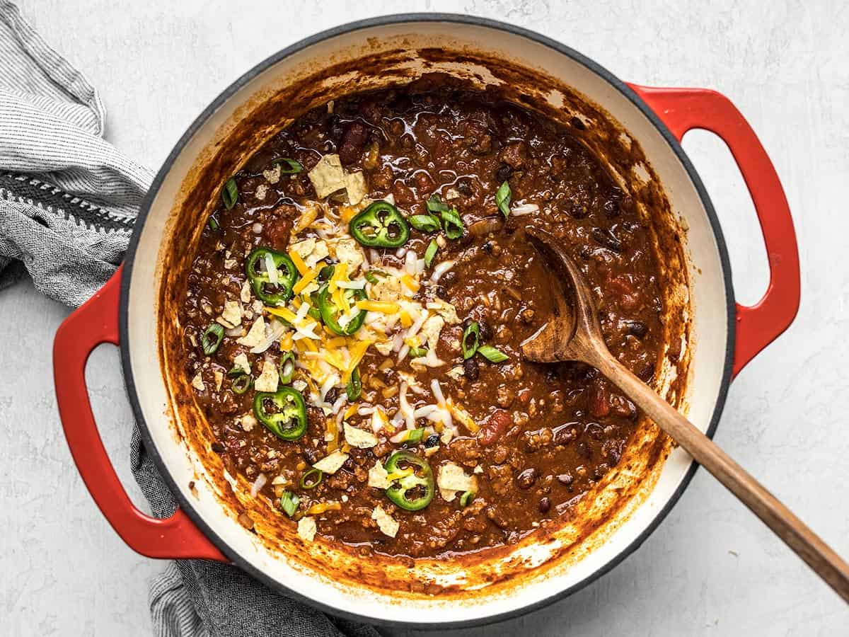 Overhead view of a pot full of chili with toppings and a wooden spoon.