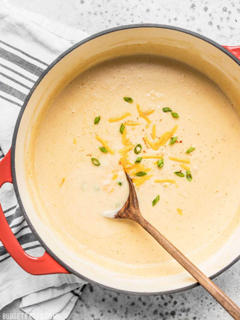 A wooden ladle spooning Cheesy Cauliflower and Potato Soup out of the pot. 