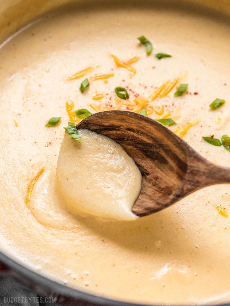 Close up of a wooden ladle in a pot of thick and creamy Cheesy Cauliflower and Potato Soup