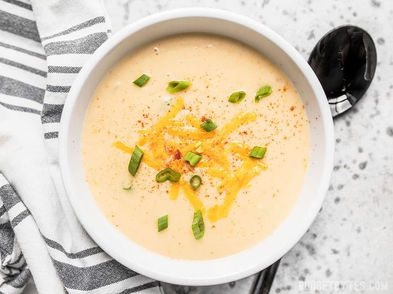 A bowl of Cheesy Cauliflower and Potato Soup with cheddar and green onion sprinkled on top. 