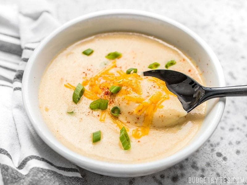A spoon scooping Cheesy Cauliflower and Potato Soup out of a bowl 