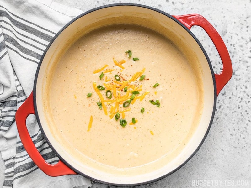 A finished pot of Cheesy Cauliflower and Potato Soup with cheddar and green onion sprinkled on top. 