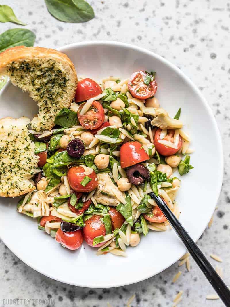 Italian Orzo Salad on a plate with a piece of garlic bread on the side.