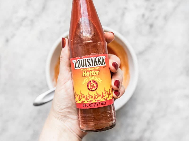 Louisiana Hot Sauce bottle being held over a bowl