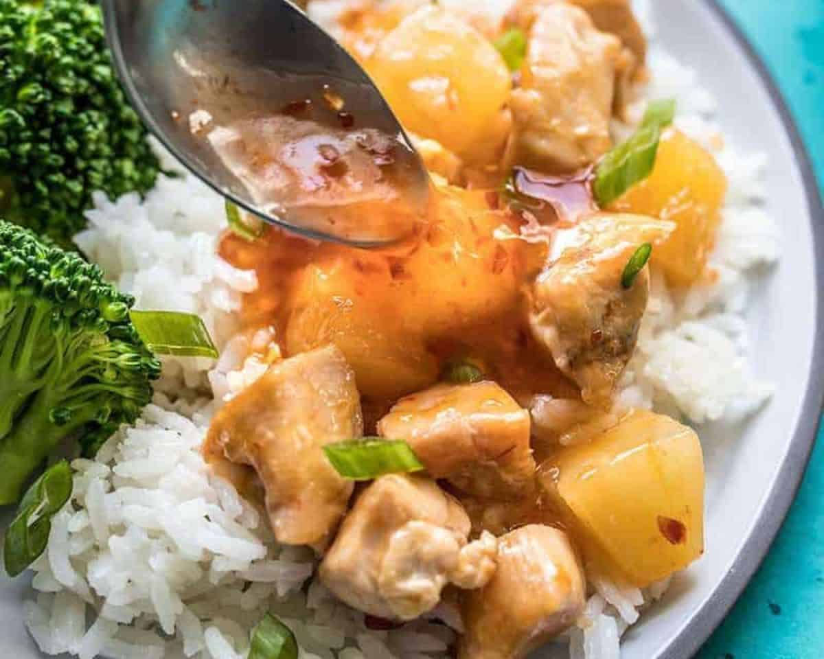 A spoon pouring sweet chili sauce over chicken with rice and broccoli.