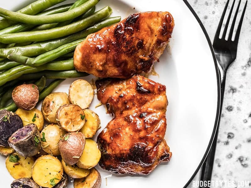 Sweet and Spicy Glazed Chicken Thighs on a plate with roasted potatoes and green beans. 