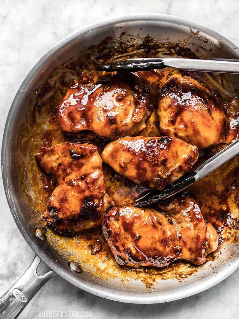 Glazed Chicken Thighs in a skillet with a pair of tongs.