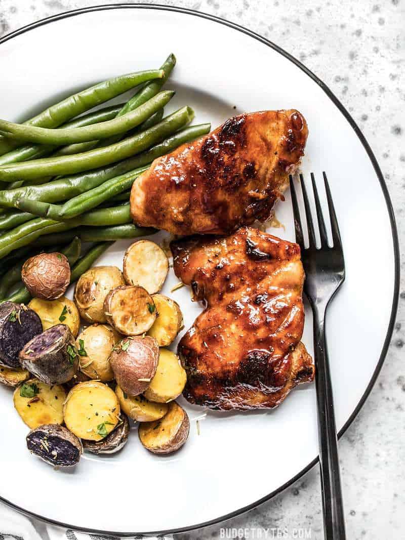 Sweet and Spicy Glazed Chicken Thighs on a plate with rosemary roasted potatoes and steamed green beans.
