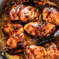 close up of glazed chicken in a skillet with tongs