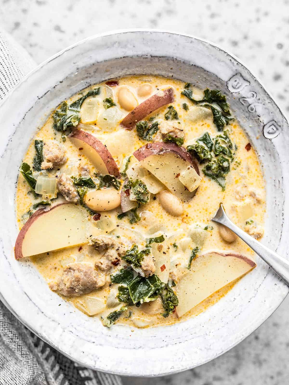 Close up overhead view of a bowl of Zuppa Toscana with a spoon in the center.