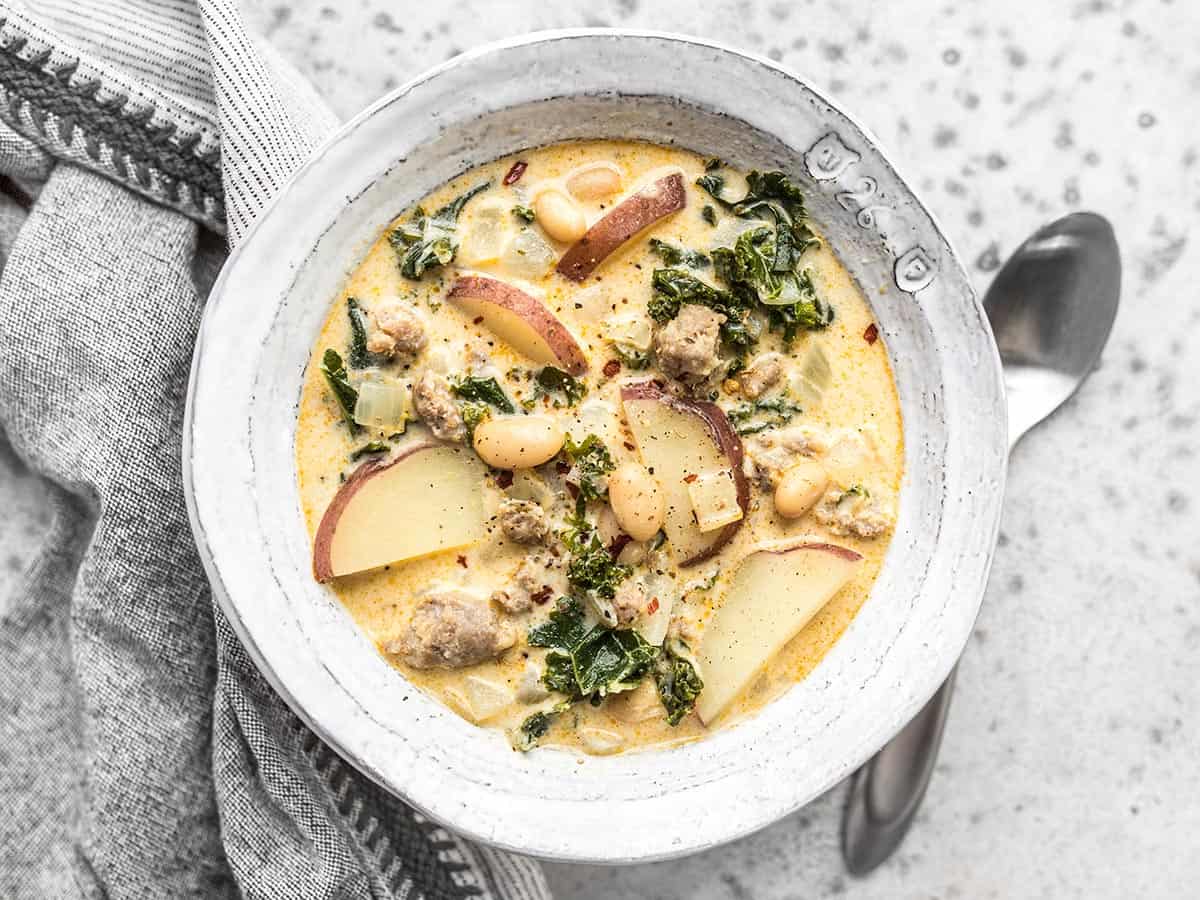 Overhead view of a bowl of zuppa toscana with a spoon on the side. 