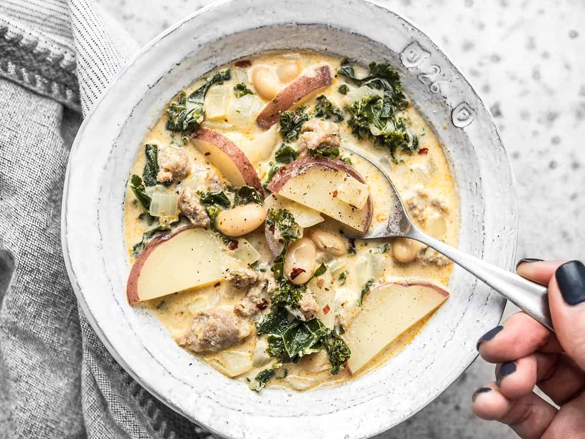 Overhead view of a bowl of Zuppa Toscana with a spoon dipping into the center. 