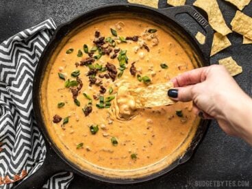 A chip being dipped into a skillet full of Spicy Chorizo Cheese Dip