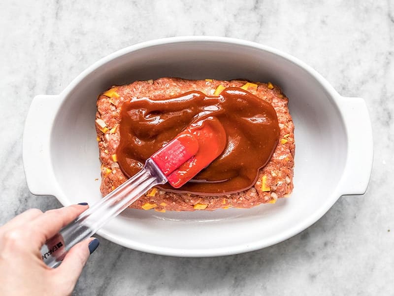 Ketchup Glaze being spread over the unbaked meatloaf in the casserole dish